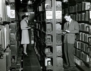 Old photo of two people browsing in the library stacks