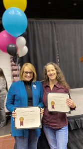 Vicki Evans and Tracy Patton of the MSU Libraries stand side-by-side displaying their Years of Service certificates with balloons in background.