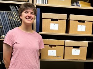 Hanna Henroid, an intern with MSU Libraries Special Collections and Archives stands next to a stack of boxed archival documents.
