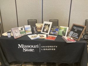 Table at Missouri Conference on History with books and magazines for sale as well as tote bags and pens, the 2022 annual report, and a sign advertising the publications.