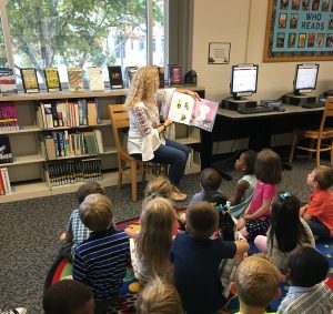 A female librarian reads to a group of schoolchildren inside of the Haseltine Library at Greenwood Laboratory School.