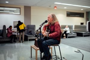 Retired librarian Craig Amason plays guitar and sings into a microphone