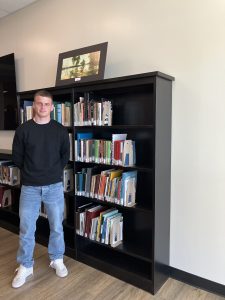 Alex Matthews stands by bookshelf in the Ozarks Room